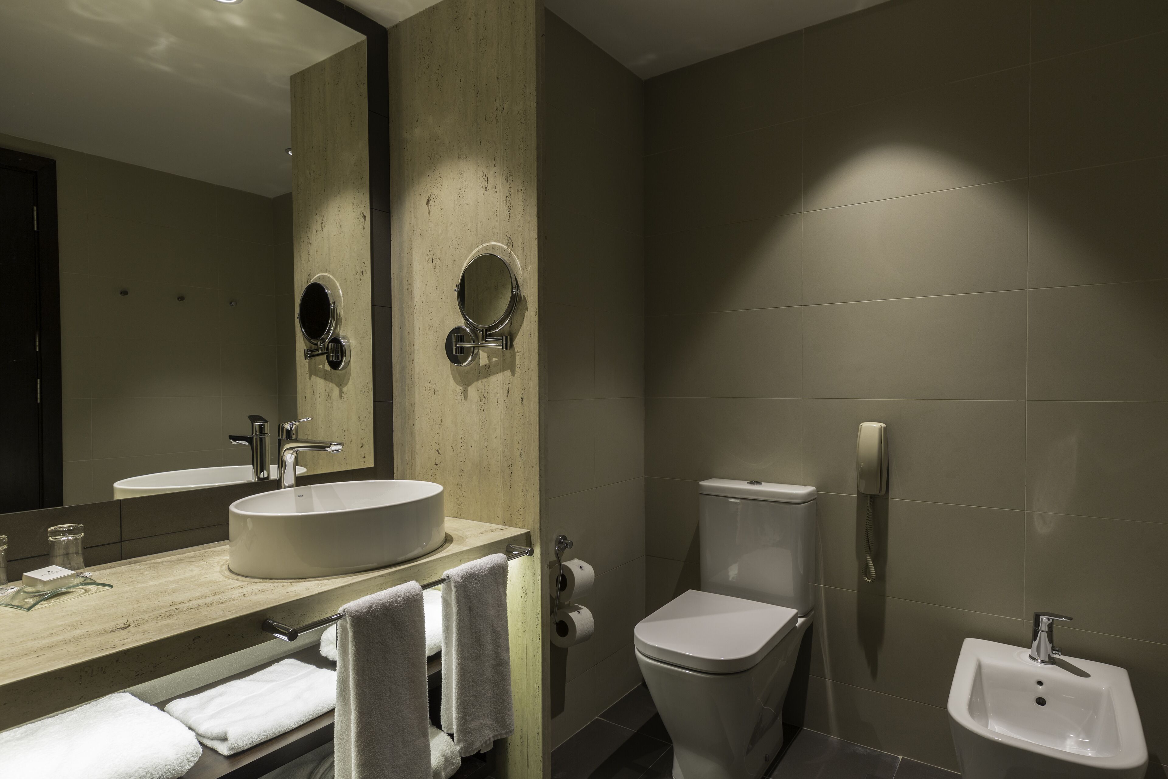 A modern bathroom with a large mirror, two sinks, a toilet, and a bidet.