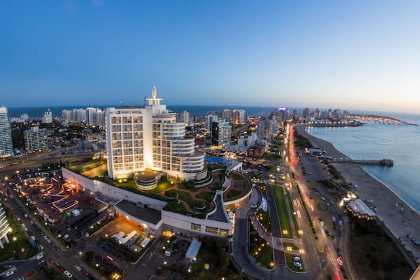 Paisagem urbana costeira com edifícios altos modernos, um porto de iates e uma área de praia bem iluminada.