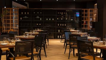 Interior de restaurante con varias mesas y sillas, una estantería con botellas de vino y una pantalla de televisión.