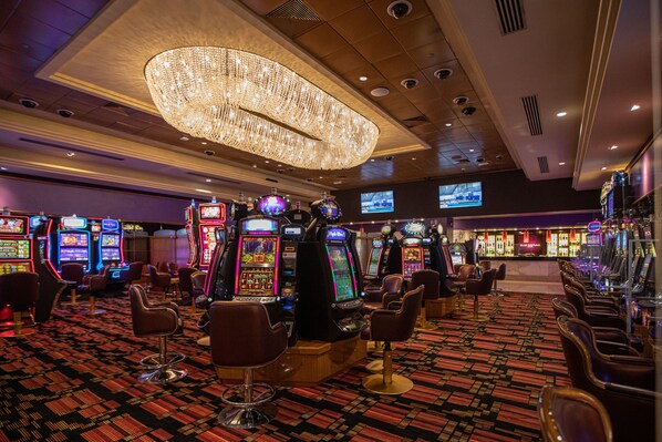 Interior de un casino con máquinas tragamonedas, zona de bar y asientos cómodos.