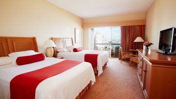 Habitación de hotel con dos camas, televisor, escritorio y vista a la ciudad.