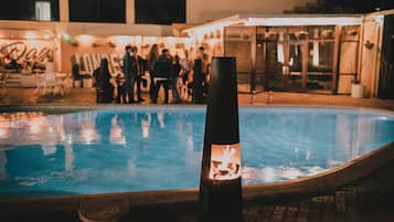 Una zona de piscina con un elemento decorativo de fuego al frente y un edificio con un letrero en el fondo.