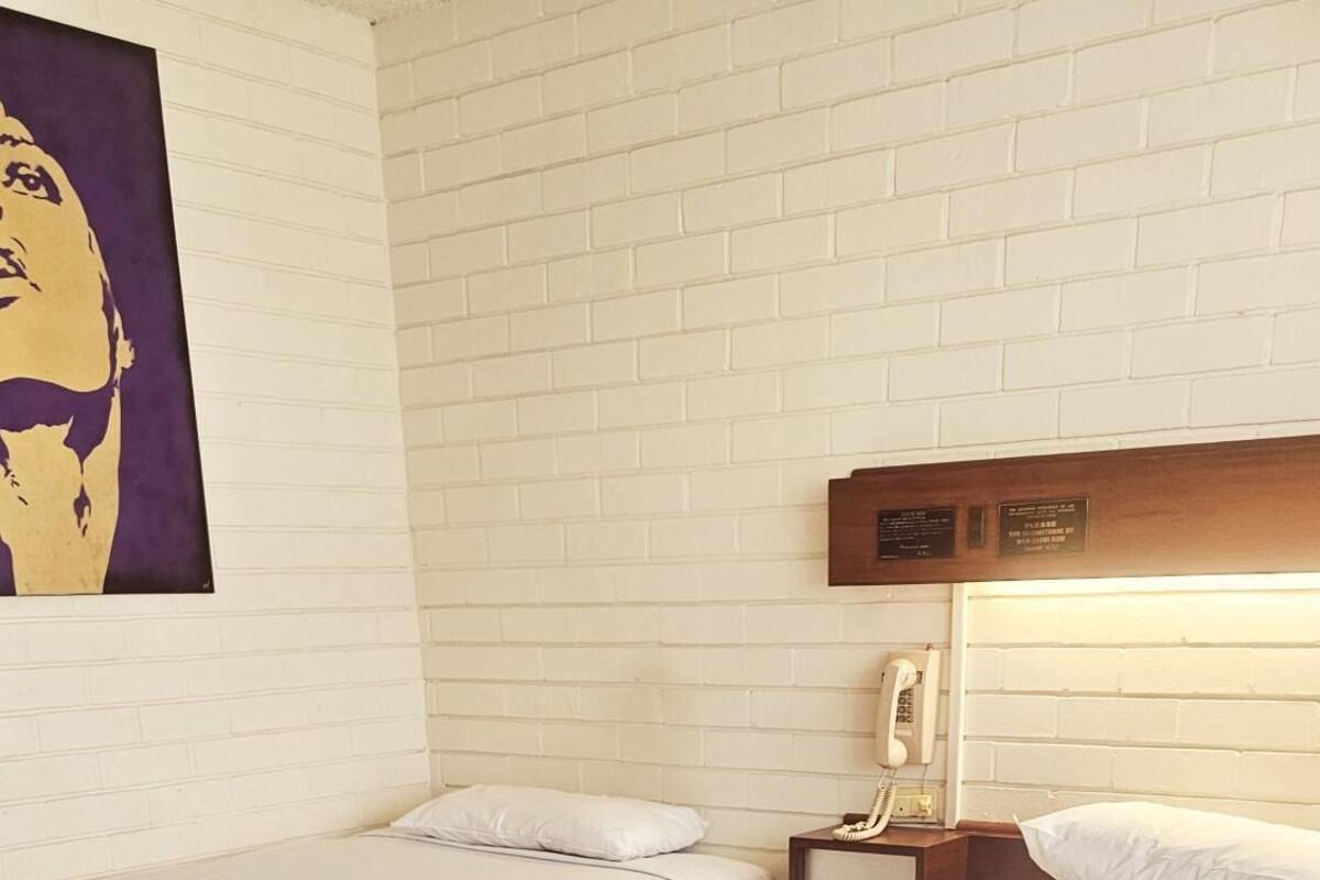 Ein Hotelzimmer mit zwei Betten, einer weißen Ziegelwand, einem Telefon und einem gemusterten Teppich.