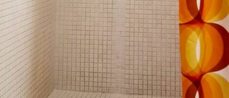 A shower with a grid-patterned tiled wall, a handheld showerhead, a handheld showerhead, a towel rack, and a shower curtain with a geometric pattern.