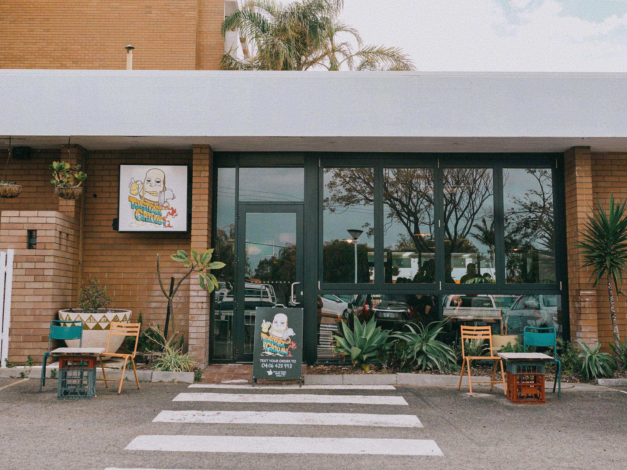 Un restaurant doté d’une grande entrée vitrée, d’une terrasse avec des chaises et d’une enseigne publicitaire affichant le menu.
