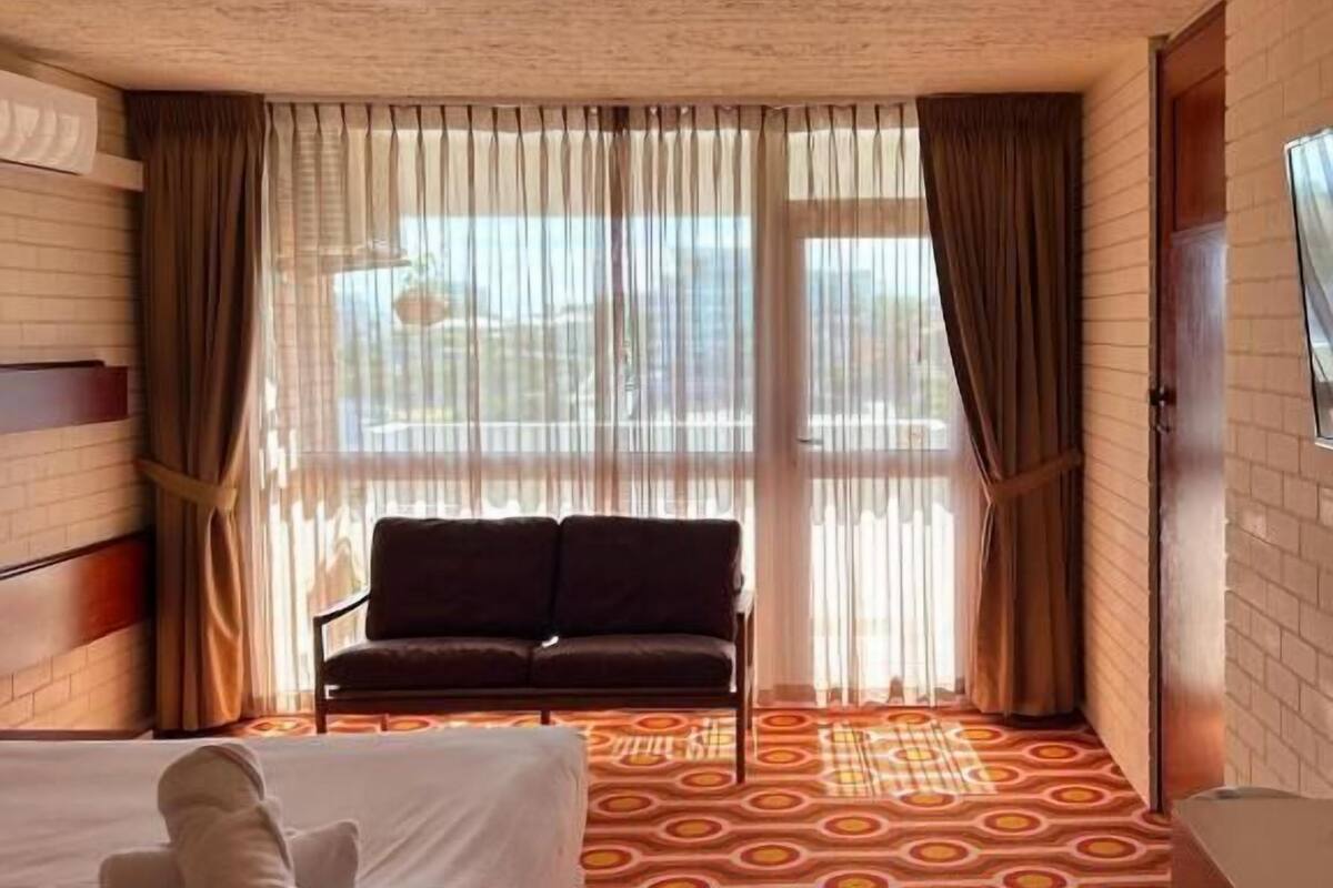 Ein Hotelzimmer mit Bett, Sofa, Fernseher und einem gemusterten Teppich.