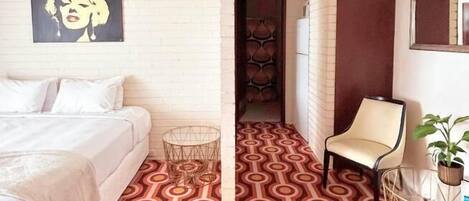 A hotel room with a bed, a chair, a small table, and a patterned floor.