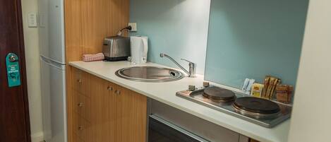 A compact kitchen with a built-in refrigerator, a coffee maker, a kettle, a sink, and a dishwasher.