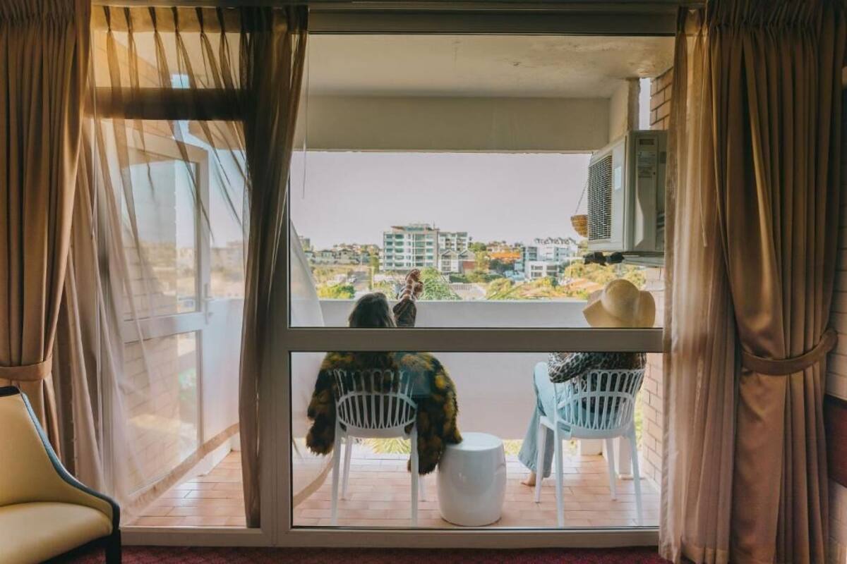 Ein Balkon mit zwei Stühlen, einem weißen Tisch und Blick auf Gebäude und Grünflächen.