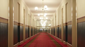 A long, narrow hallway with a red carpet, white walls, and a chandelier. - Grand Hotel Melbourne (Docklands)