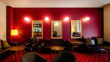 Un hall de hotel con alfombra roja, sofás de cuero, sillones y una mesa de madera.
