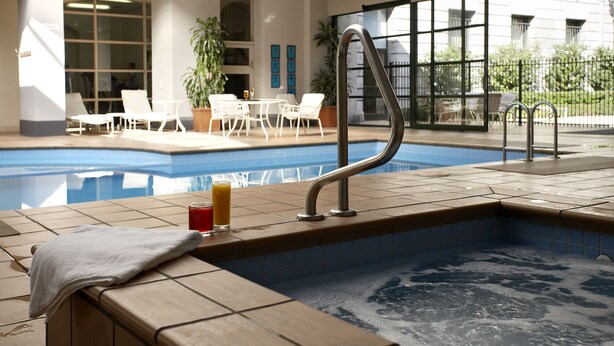An indoor swimming pool with a hot tub, lounge chairs, and a table with drinks. - Grand Hotel Melbourne (Docklands)