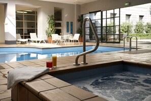 An indoor swimming pool with a hot tub, lounge chairs, and a table with drinks. - Grand Hotel Melbourne (Docklands)