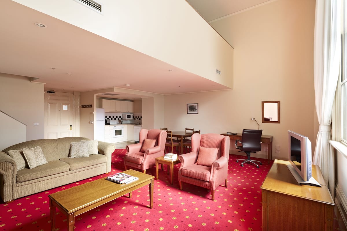 A living room with a sofa, two armchairs, a coffee table, a TV on a wooden stand, and a red carpet.