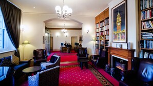 A hotel lobby with a red carpet, leather armchairs, a fireplace, and a bookshelf. - Grand Hotel Melbourne (Docklands)