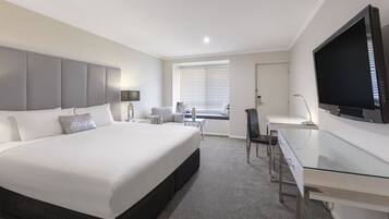Ein modernes Hotelzimmer mit einem großen Bett, einem Schreibtisch, einem Fernseher und einem Fenster mit Jalousien.