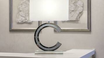 A modern lamp with a metallic base and a white shade on a white table.