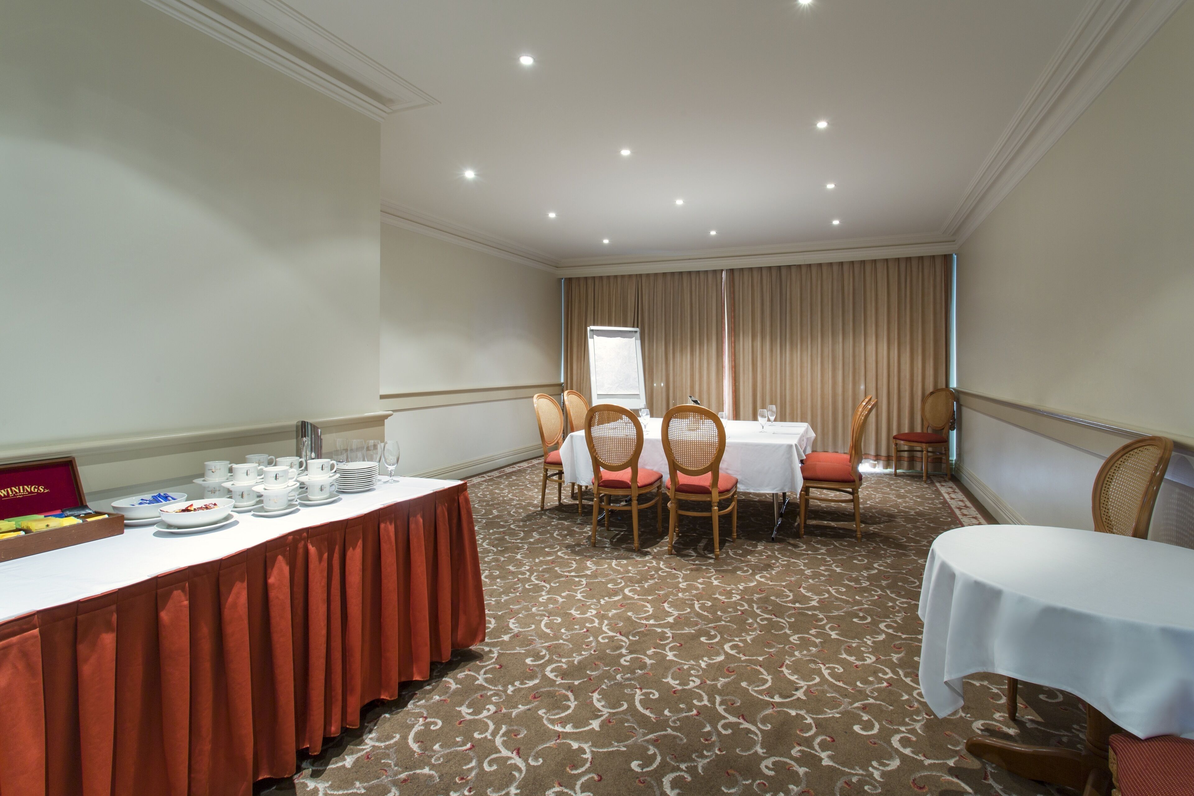 Uma sala de conferência com uma mesa comprida, cadeiras e uma mesa de buffet com pratos e copos.