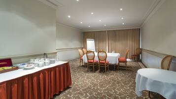 Uma sala de conferência com uma mesa comprida, cadeiras e uma mesa de buffet com pratos e copos.