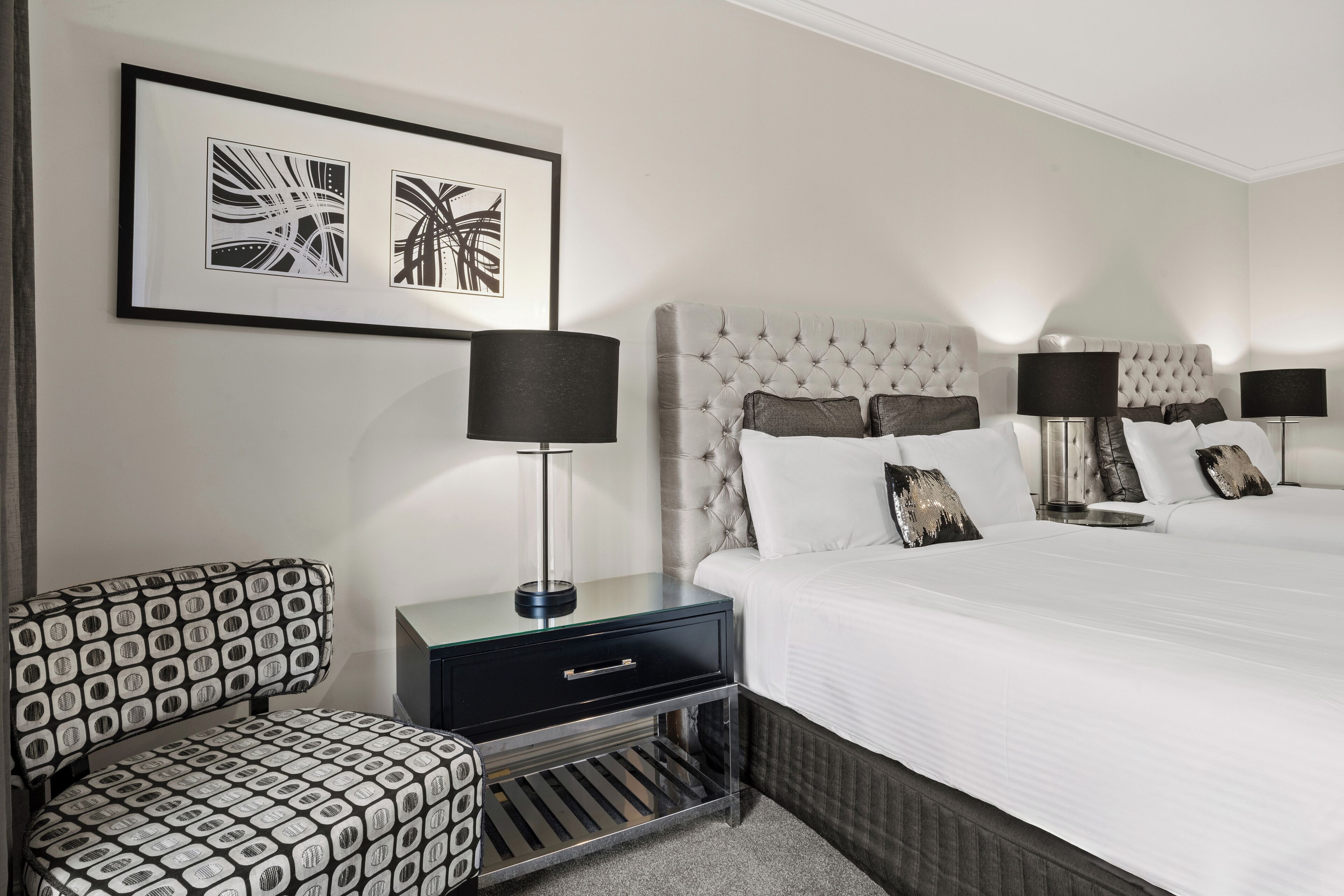 Een hotelkamer met een groot bed, twee nachtkastjes met lampen, een stoel en een wanddecoratie in een lijst.