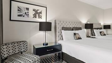 Een hotelkamer met een groot bed, twee nachtkastjes met lampen, een stoel en een wanddecoratie in een lijst.