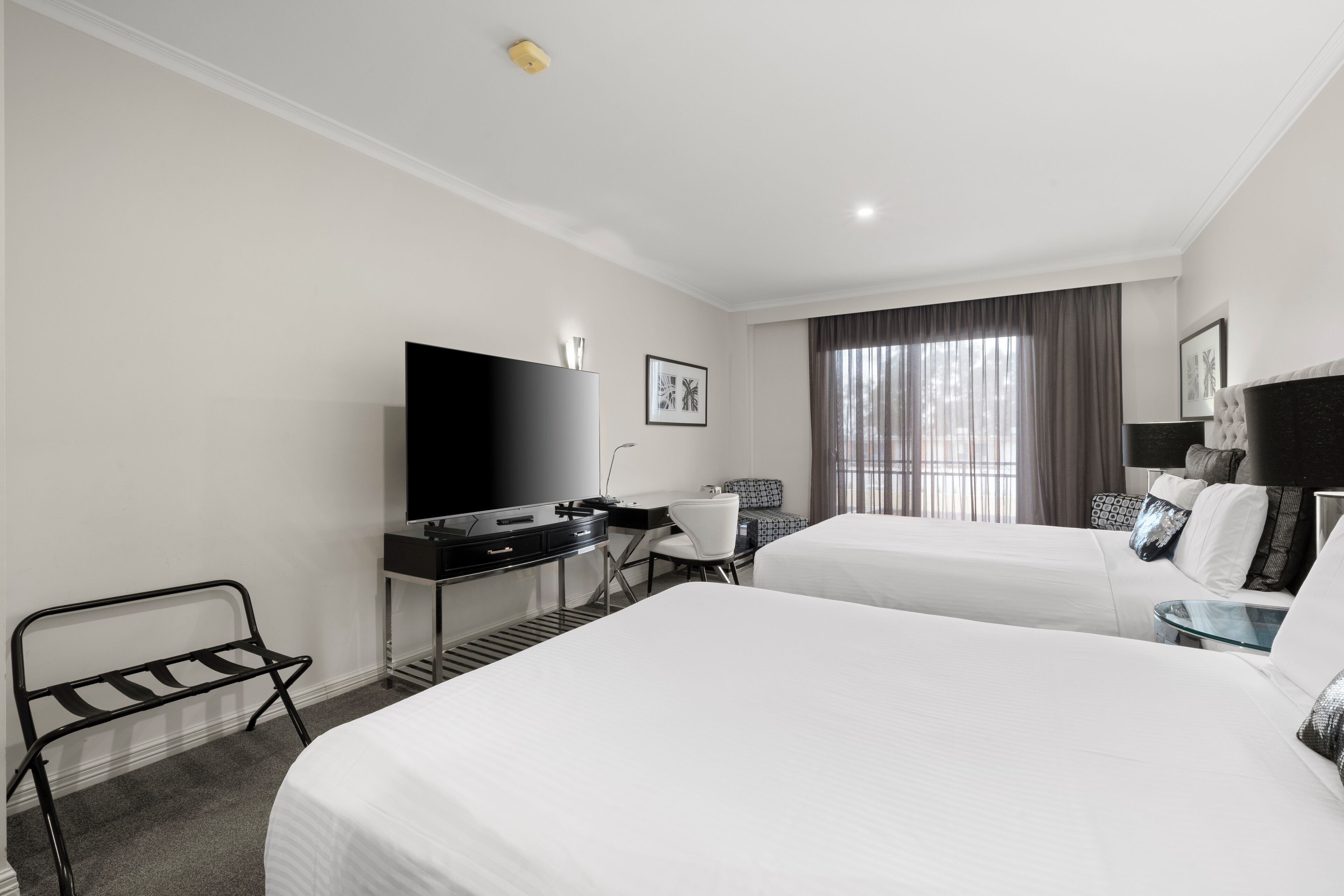 Habitación de hotel con dos camas, un escritorio, televisor de pantalla plana, una silla y una ventana con cortinas.