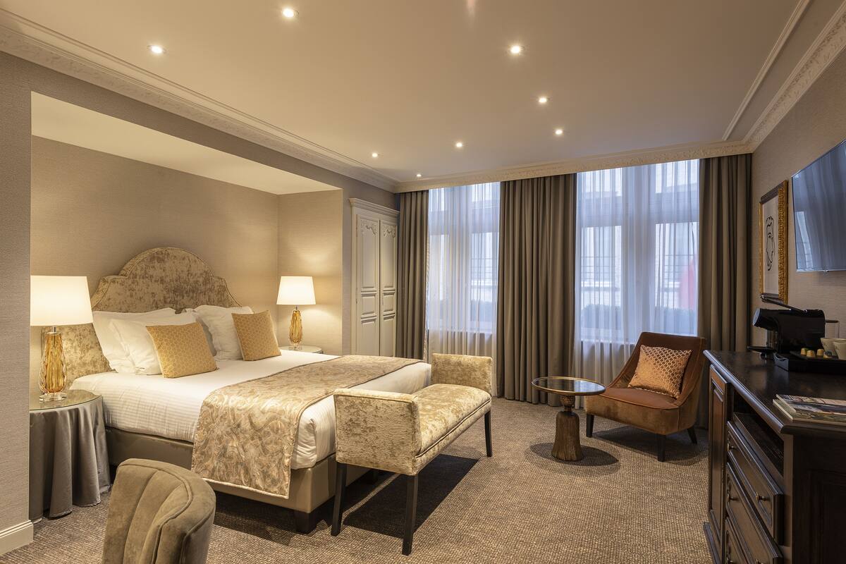 Een hotelkamer met een groot bed, twee nachtkastjes, een stoel, een klein rond tafeltje en een kaptafel.