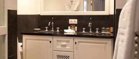 A modern bathroom with a double sink, a large mirror, and a robe hanging on the wall.