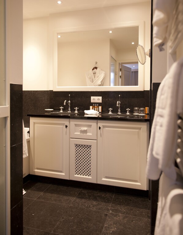 A modern bathroom with a double sink, a large mirror, and a robe hanging on the wall.