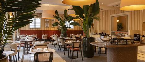 A hotel lobby with multiple dining tables, chairs, and large potted plants.