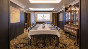 A conference room with a long table, chairs, a projector screen displaying "HOTEL PRINSENHOF", and a patterned carpet. -  Dukes’ Palace Residence – by Dukes’ Hotel Collection (Bruges)