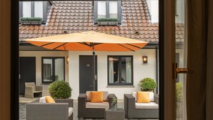 An outdoor seating area with wicker furniture, a large umbrella, and a tiled patio. -  Dukes’ Palace Residence – by Dukes’ Hotel Collection (Bruges)