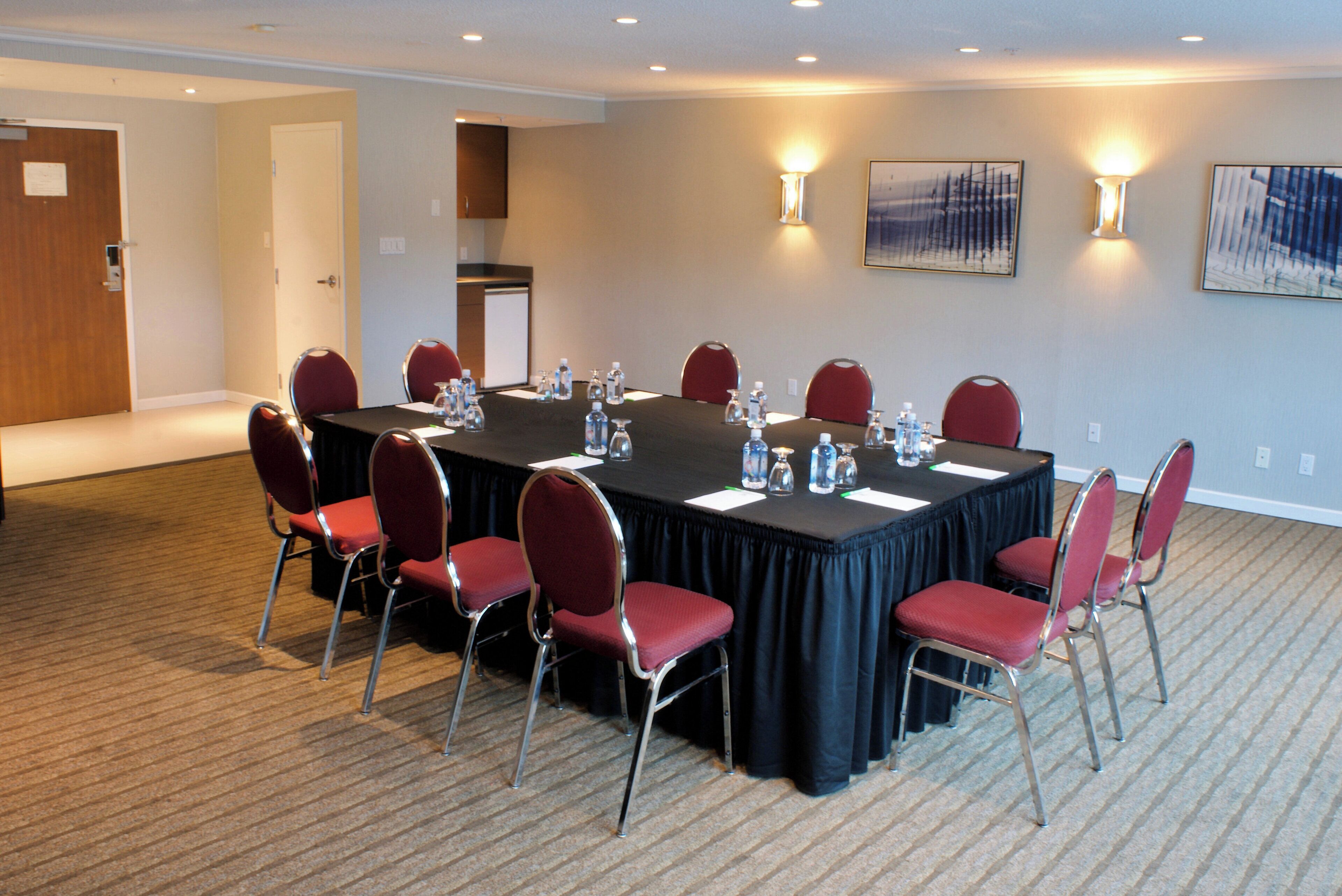 A conference room with a long table, red chairs, water bottles, and a projector screen.