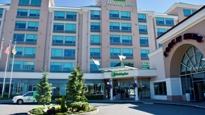 Un hotel Holiday Inn con fachada moderna, múltiples ventanas y una bandera en la parte superior.