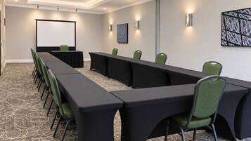 Un salón de conferencias con una larga mesa, sillas, una pantalla de proyector y luces fijadas a la pared.