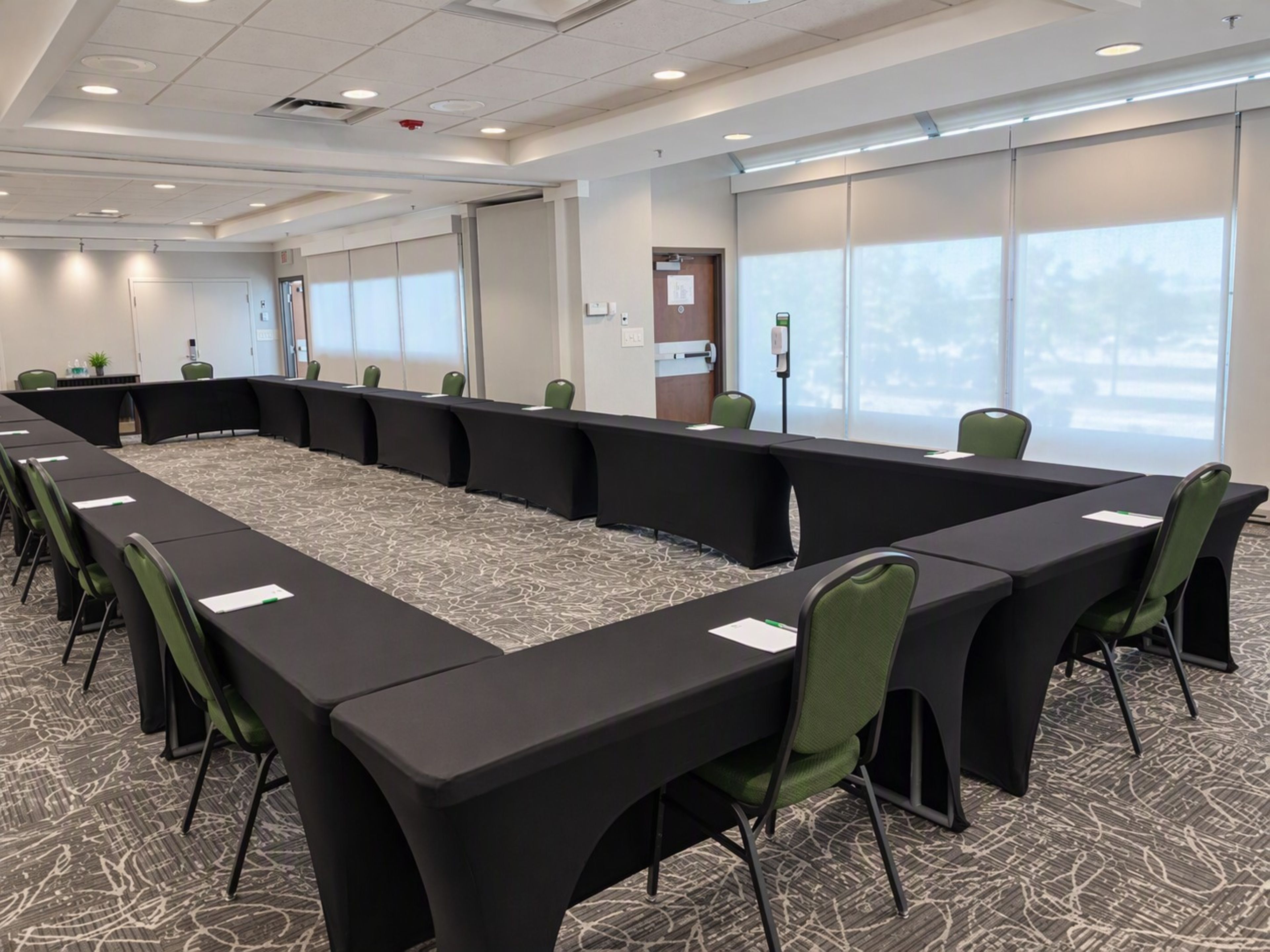 A conference room with a long table, green chairs, and carpeted flooring.