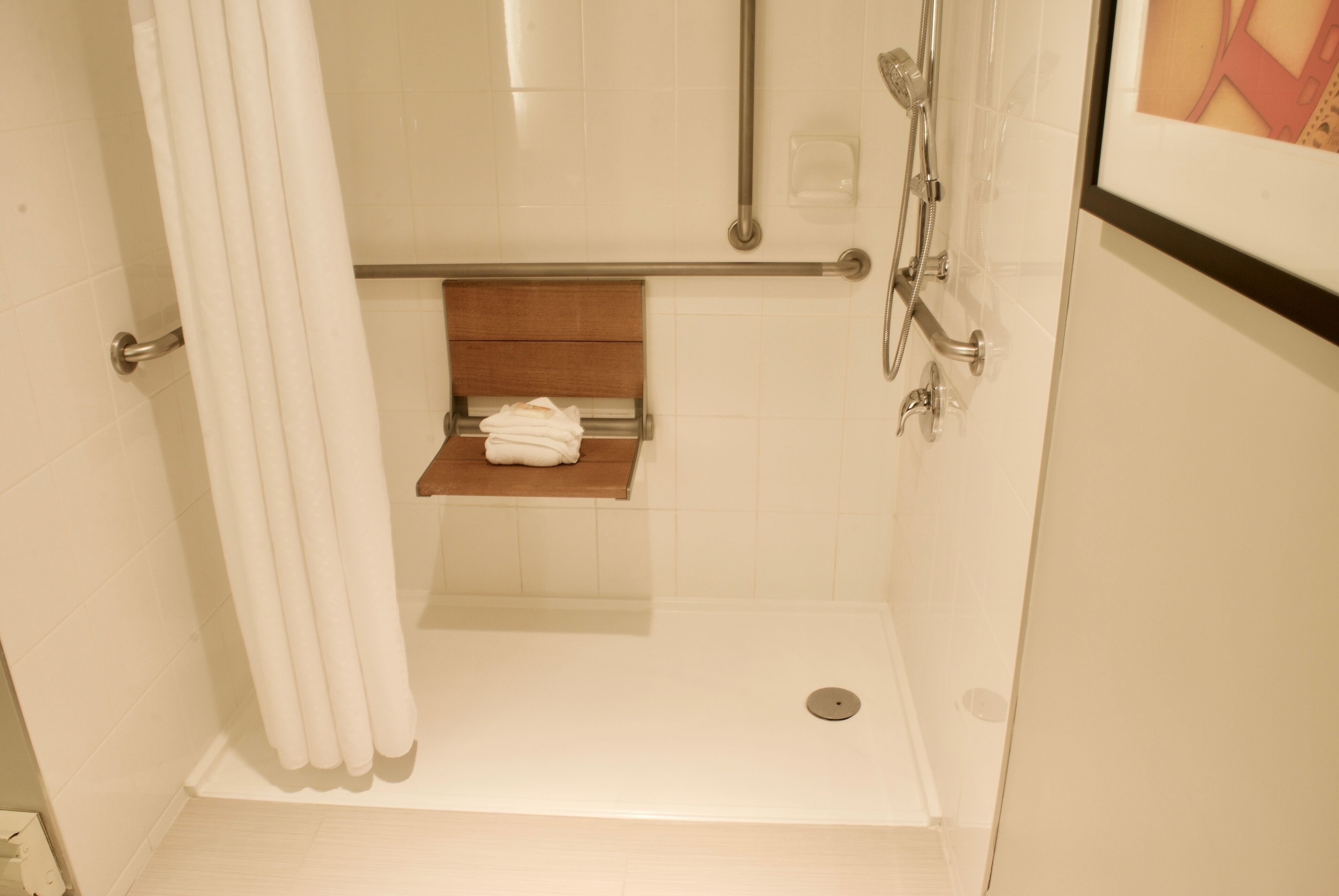 A walk-in shower with a wooden shelf holding a towel, a handrail, and a showerhead.