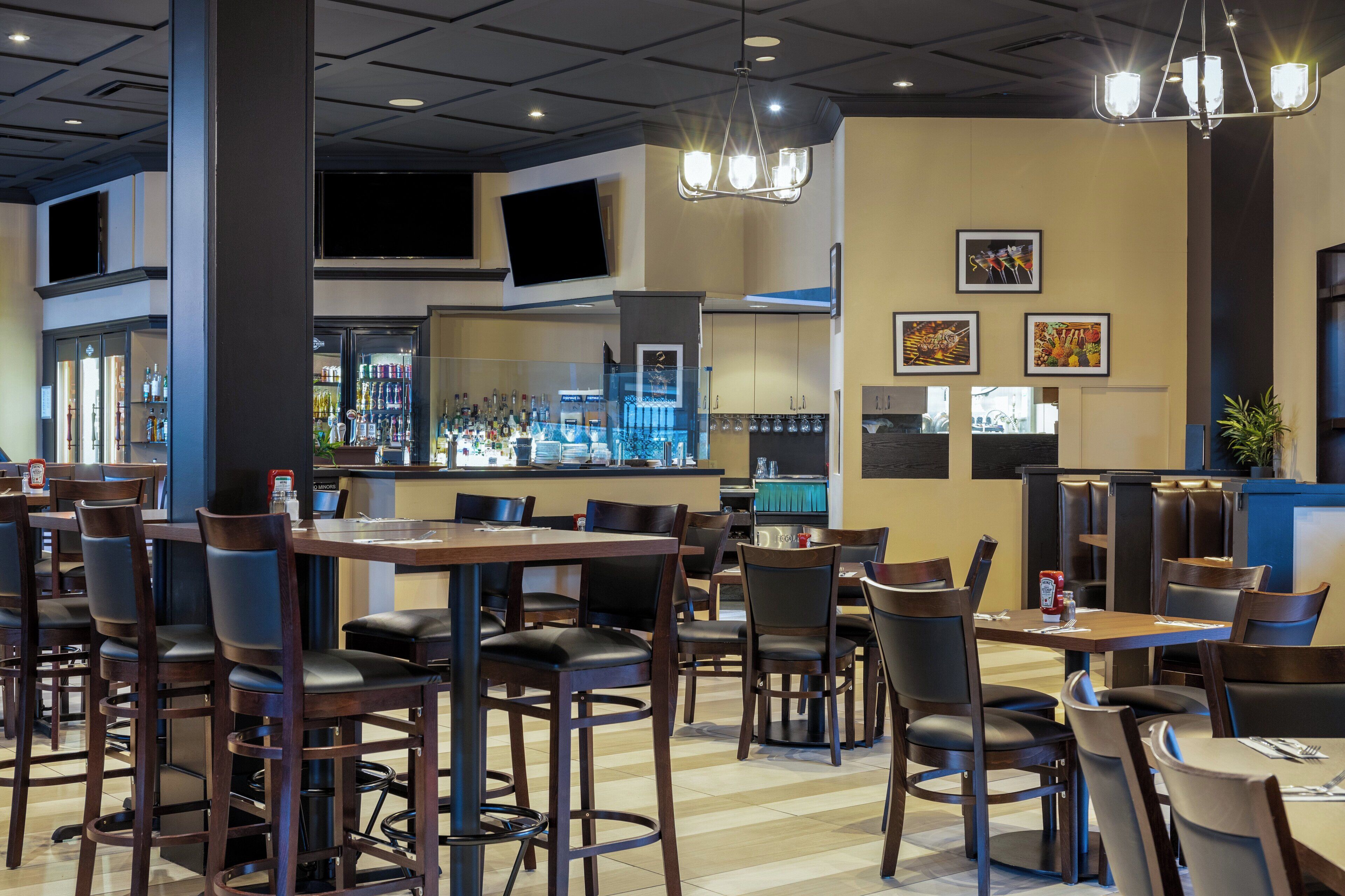A restaurant with multiple tables and chairs, a bar area with a counter, and a television mounted on the wall.