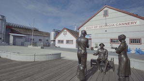 A wooden boardwalk with bronze statues of two men and a child. In the background, there's a building labeled "Gulf of Georgia Cannery" with a red roof and white walls. - Holiday Inn Vancouver Airport- Richmond by IHG (Richmond)