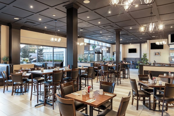 A spacious restaurant with high ceilings, modern lighting, and large windows offering views of the outside. - Holiday Inn Vancouver Airport- Richmond by IHG (Richmond)