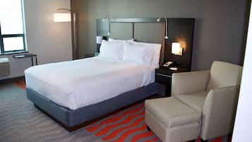 A hotel room with a large bed, a chair, a nightstand, a lamp, and a window.