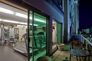 A gym with exercise equipment, a glass wall, and a small outdoor seating area with a table and chairs. - Holiday Inn Vancouver Airport- Richmond by IHG (Richmond)