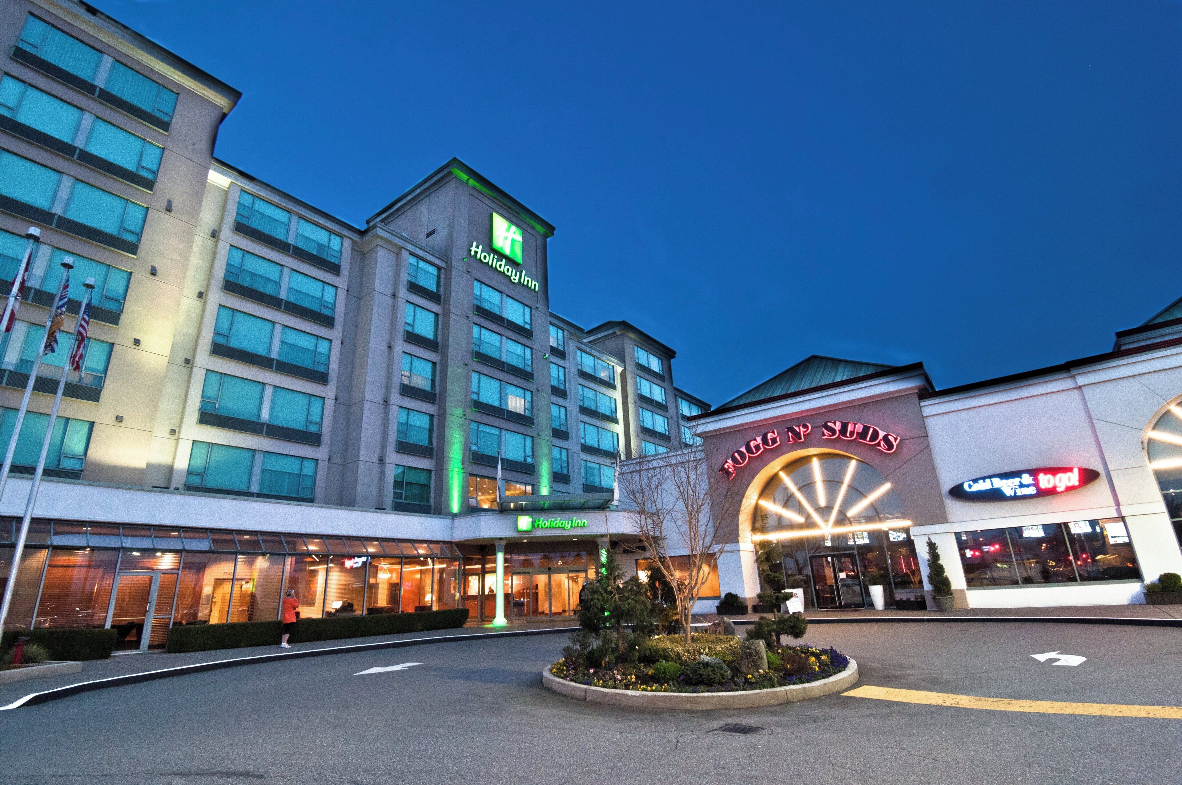 A Holiday Inn hotel with a modern design, located next to a Tugg on SUDS store.