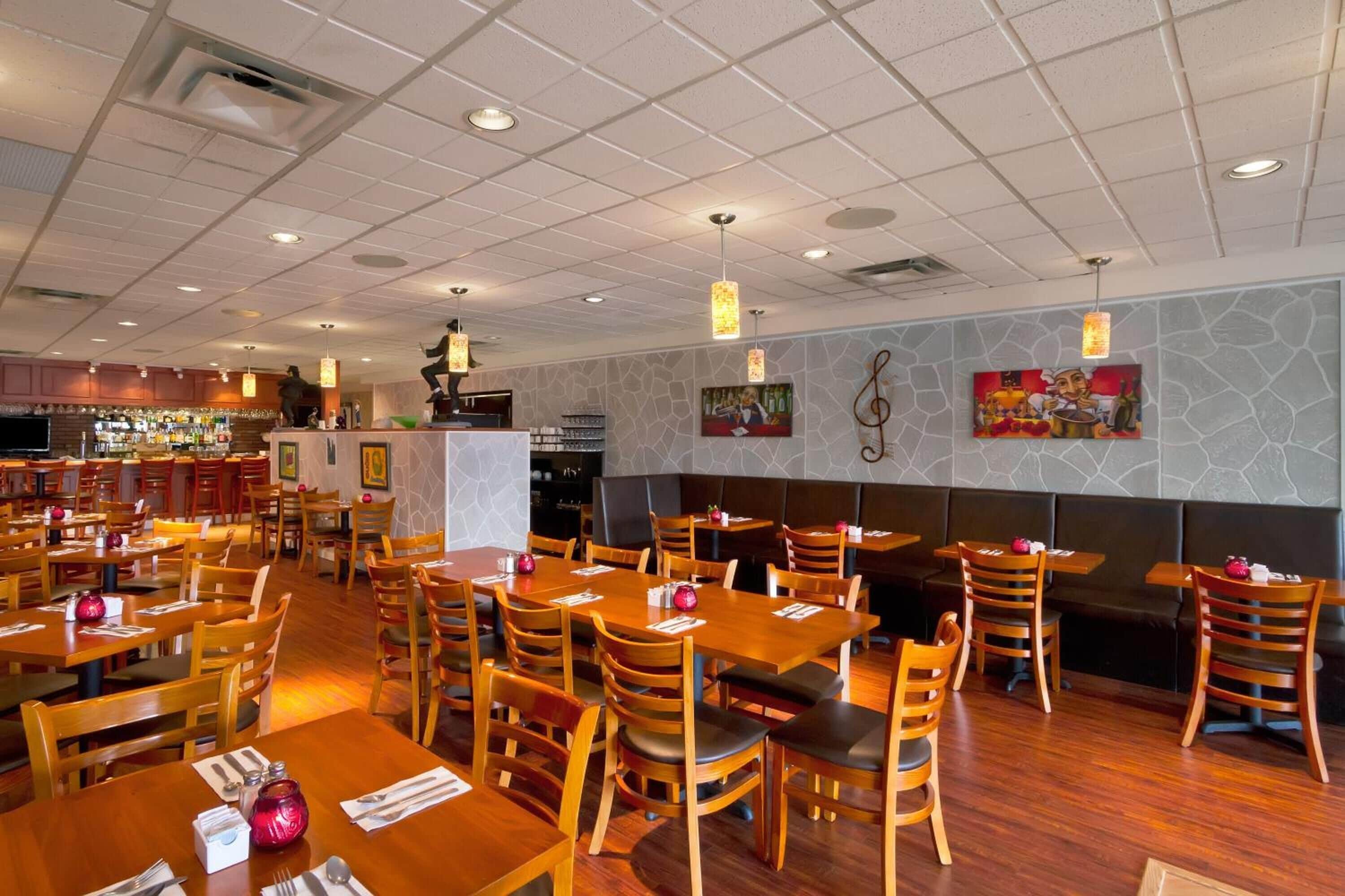 A restaurant with wooden tables and chairs, a bar area, and a stone wall with artwork.