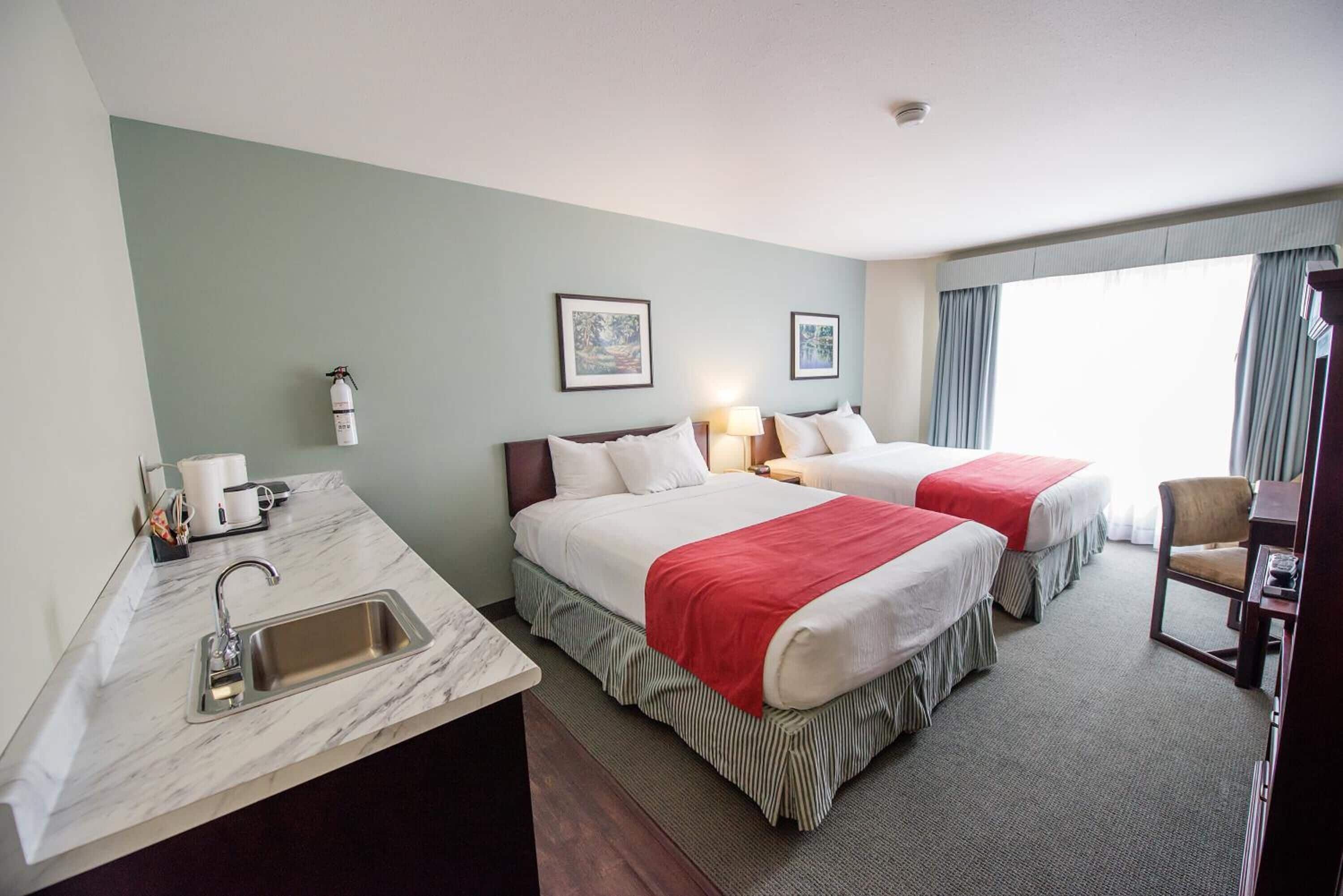 A hotel room with two beds, a sink, a chair, and a window with curtains.