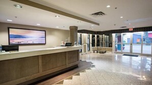 Un espace d’accueil d’hôtel comprenant un comptoir de réception, un grand tableau encadré au mur et une vue sur l’extérieur à travers les portes vitrées.