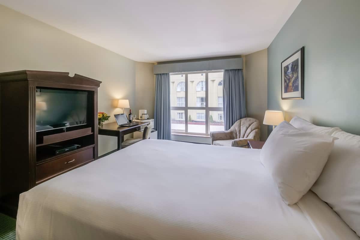 A hotel room with a large bed, a desk with a laptop, a television, and a window with curtains.
