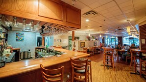 L’intérieur d’un restaurant avec un bar en bois et un espace salon, une cuisine en arrière-plan et une décoration murale colorée.