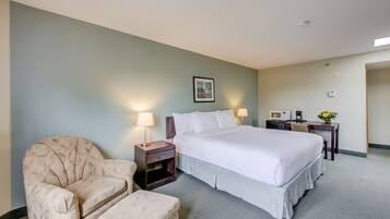 A hotel room with a bed, a chair, a small table with a lamp, a microwave, and a picture on the wall.