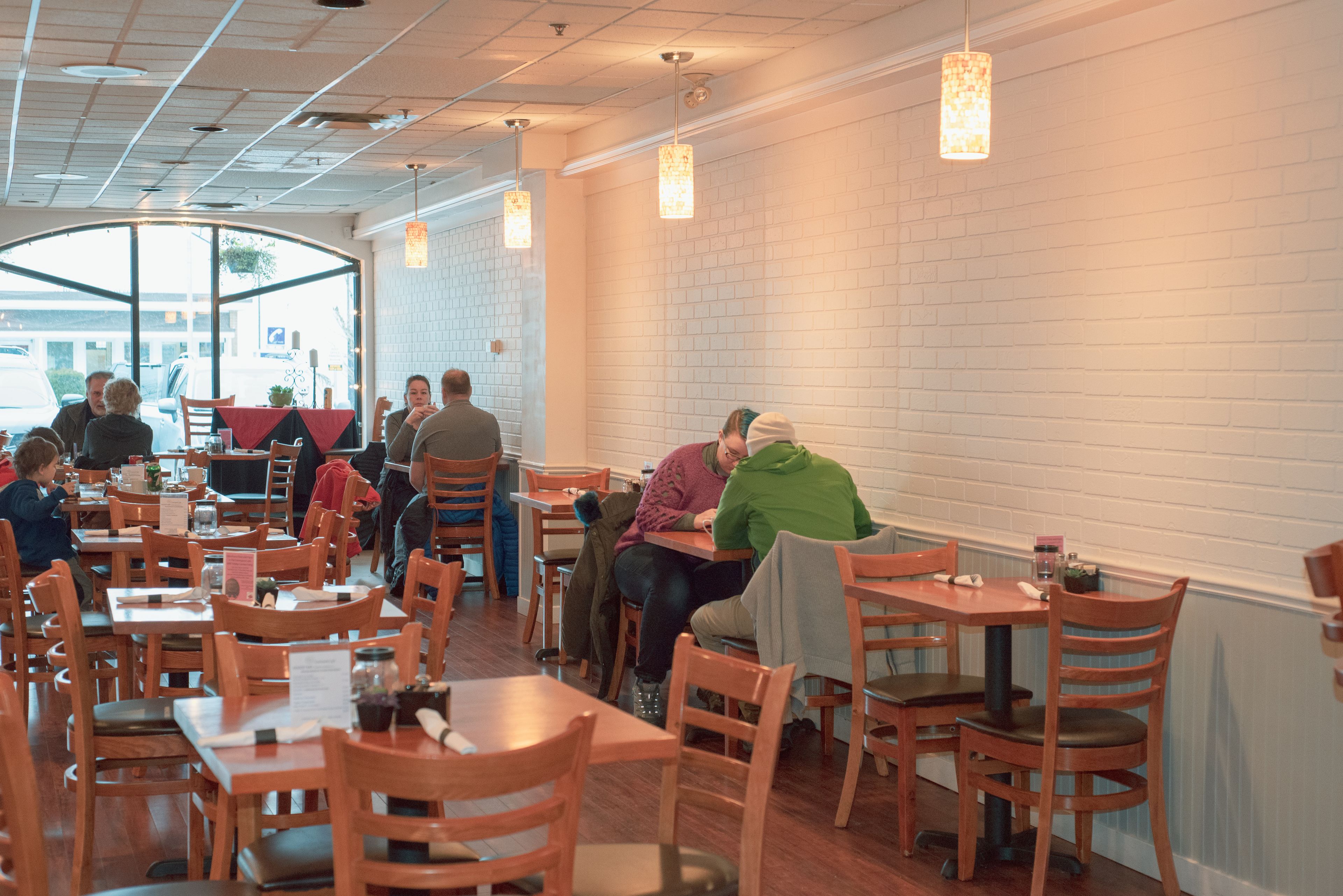 A restaurant with wooden tables and chairs, white brick walls, and pendant lighting.